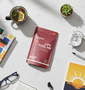 Red package labeled 'Bronn Life Fuel NR' on a white surface with a cup of tea, alarm clock, and books.