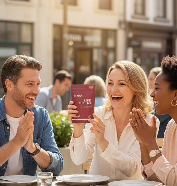 Three people sitting at a table outdoors, with one holding a product package.