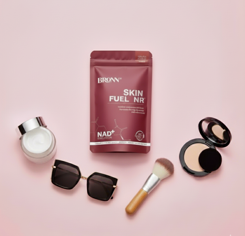 Makeup and skincare products including a brush, cream, compact, and sunglasses on a beige background.