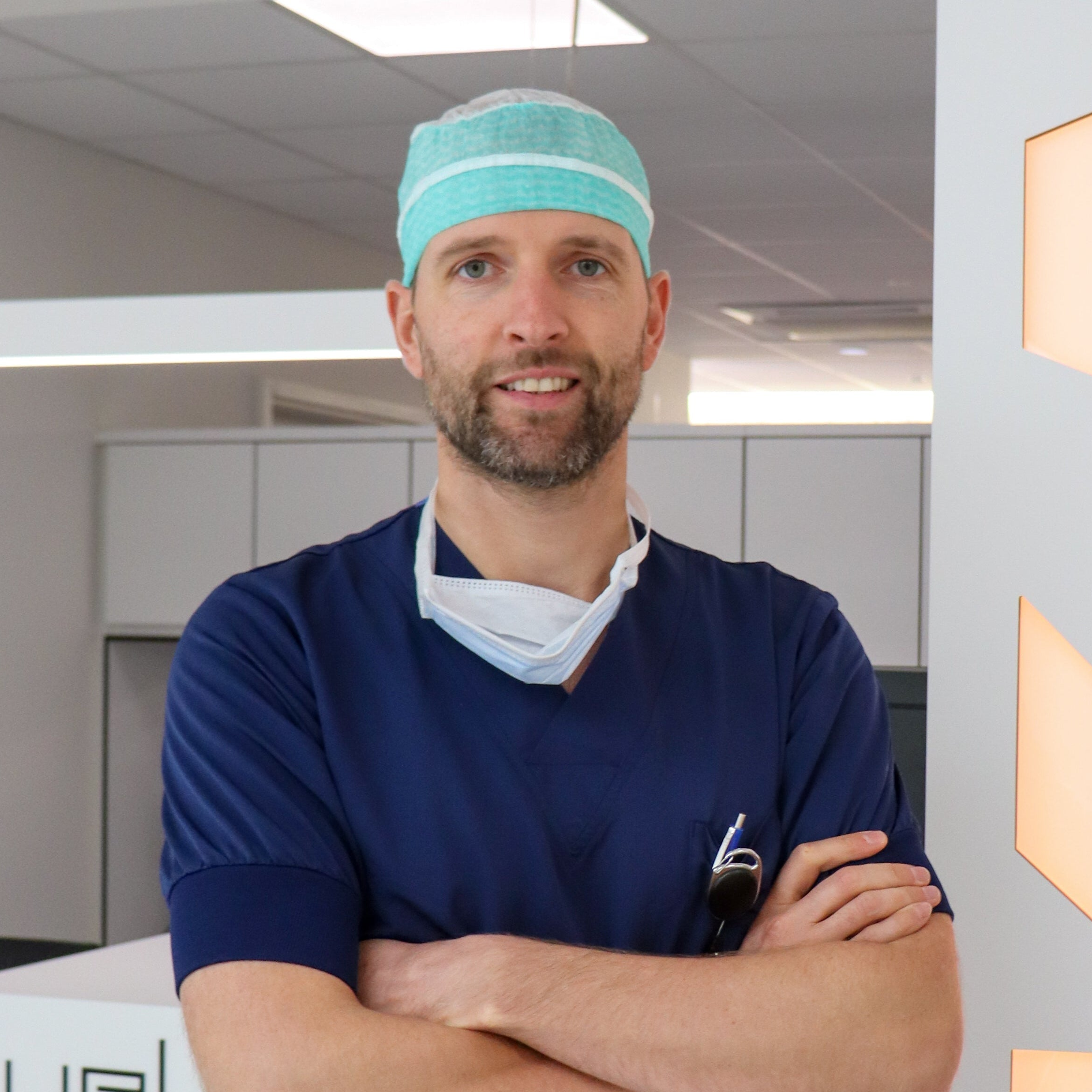 Person wearing medical scrubs with a teal headband and surgical mask in an office setting.