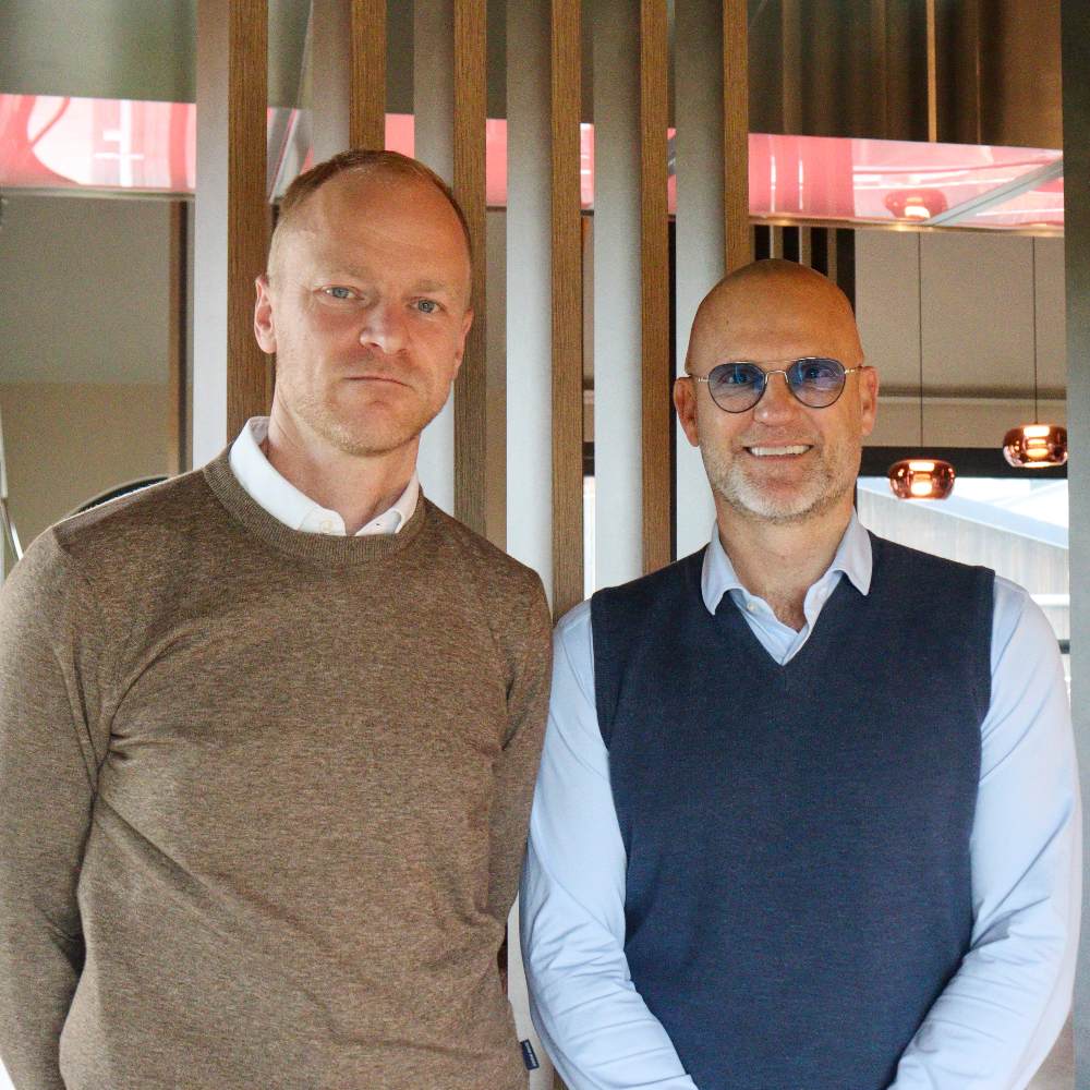Two men standing side by side indoors with a neutral background