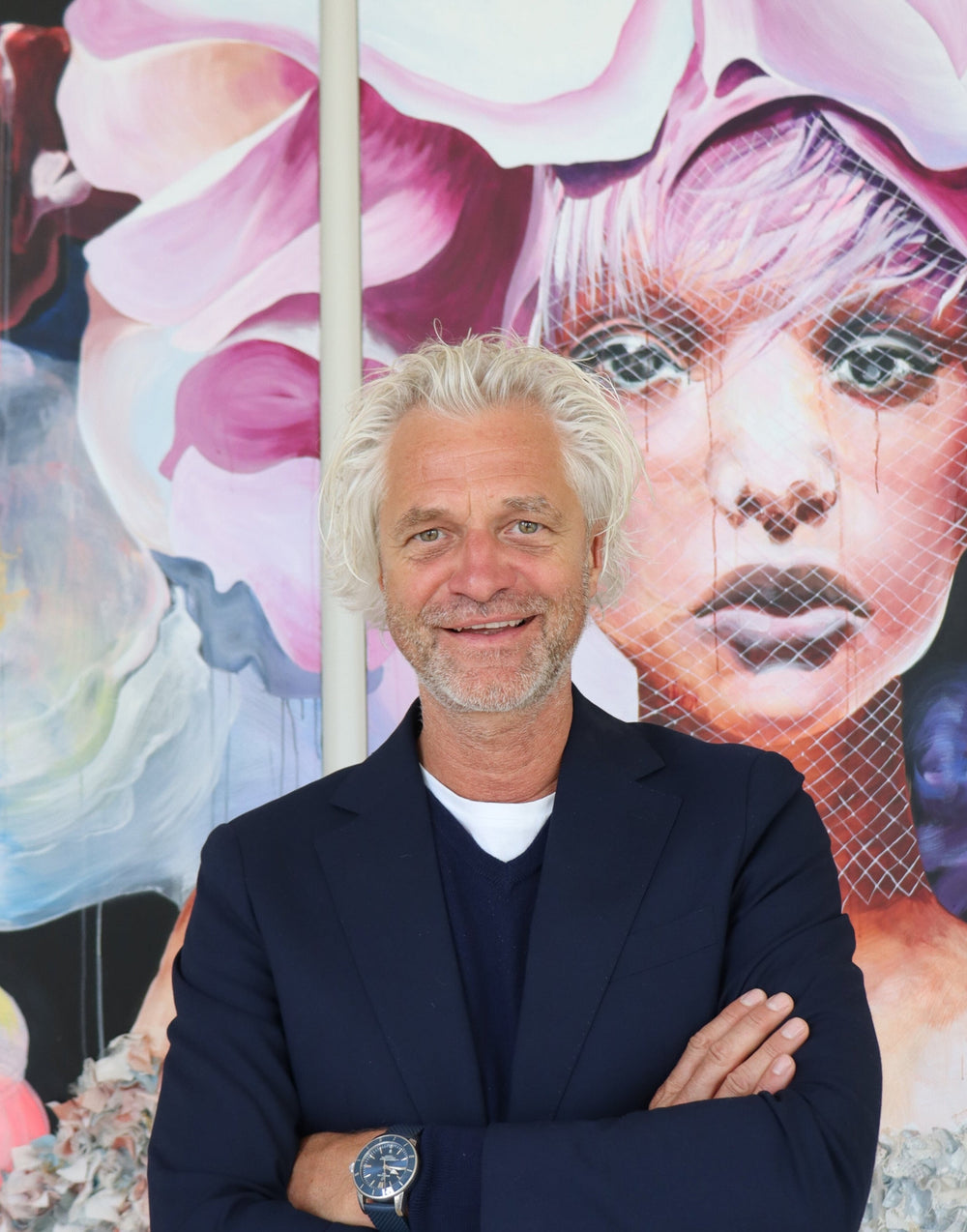 Man with gray hair standing in front of a colorful mural with artistic depiction of a face.