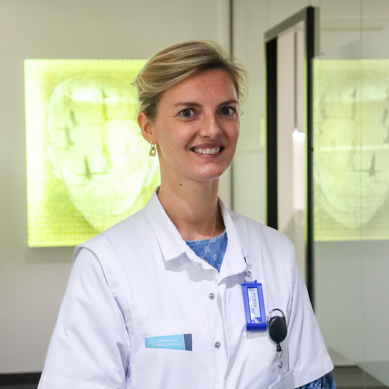 Person wearing a white lab coat with a name tag in an indoor setting