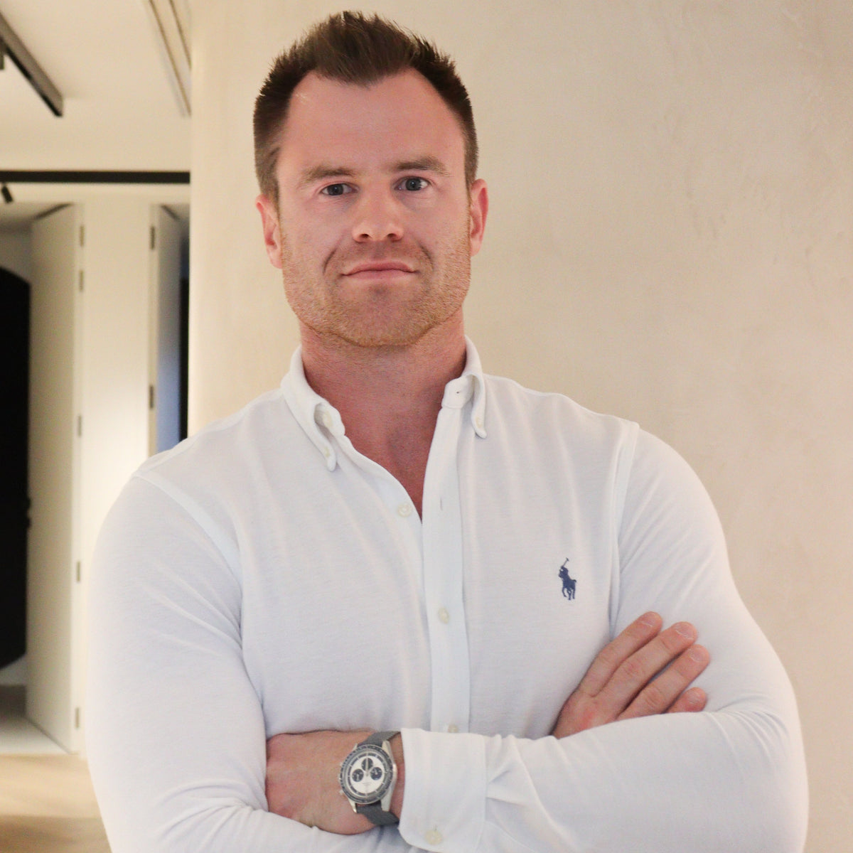 Man wearing a white Polo shirt with a logo, standing indoors. Philip Thys.