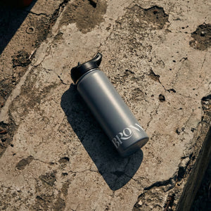 Gray water bottle with 'BRON' branding on a textured concrete surface