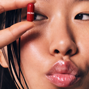 Close-up of a person holding a red BRONN bottle near their eye.