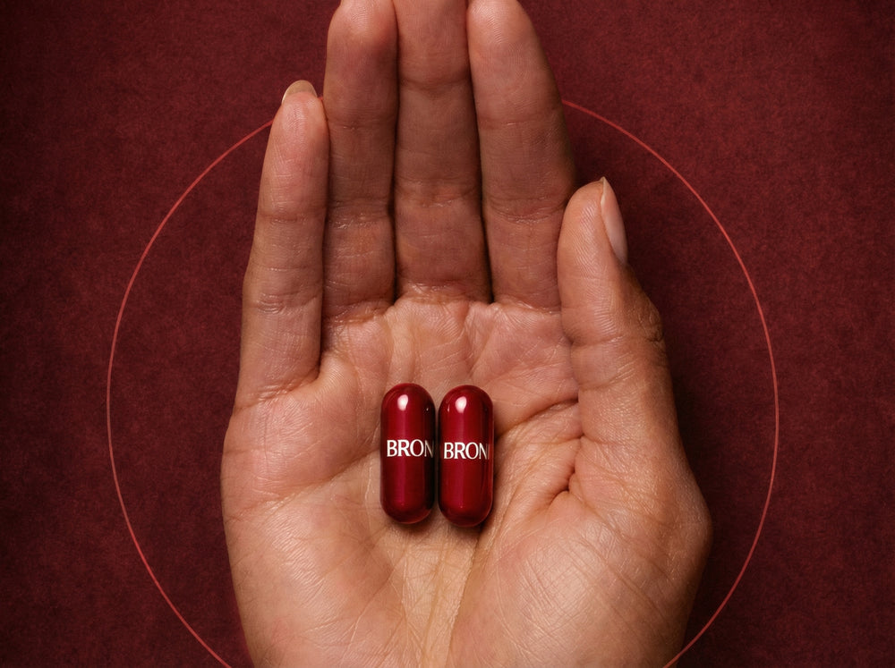 Two red capsules with 'Browns' branding held in a hand against a red background