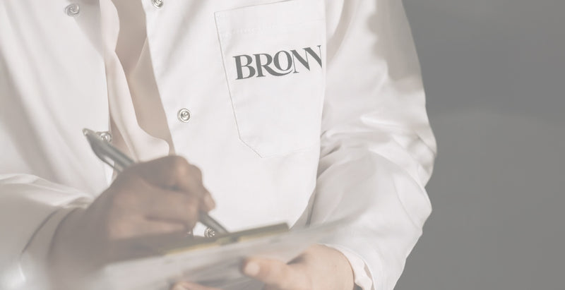 Person wearing a white coat with 'BRONN' printed on it, holding a tray.