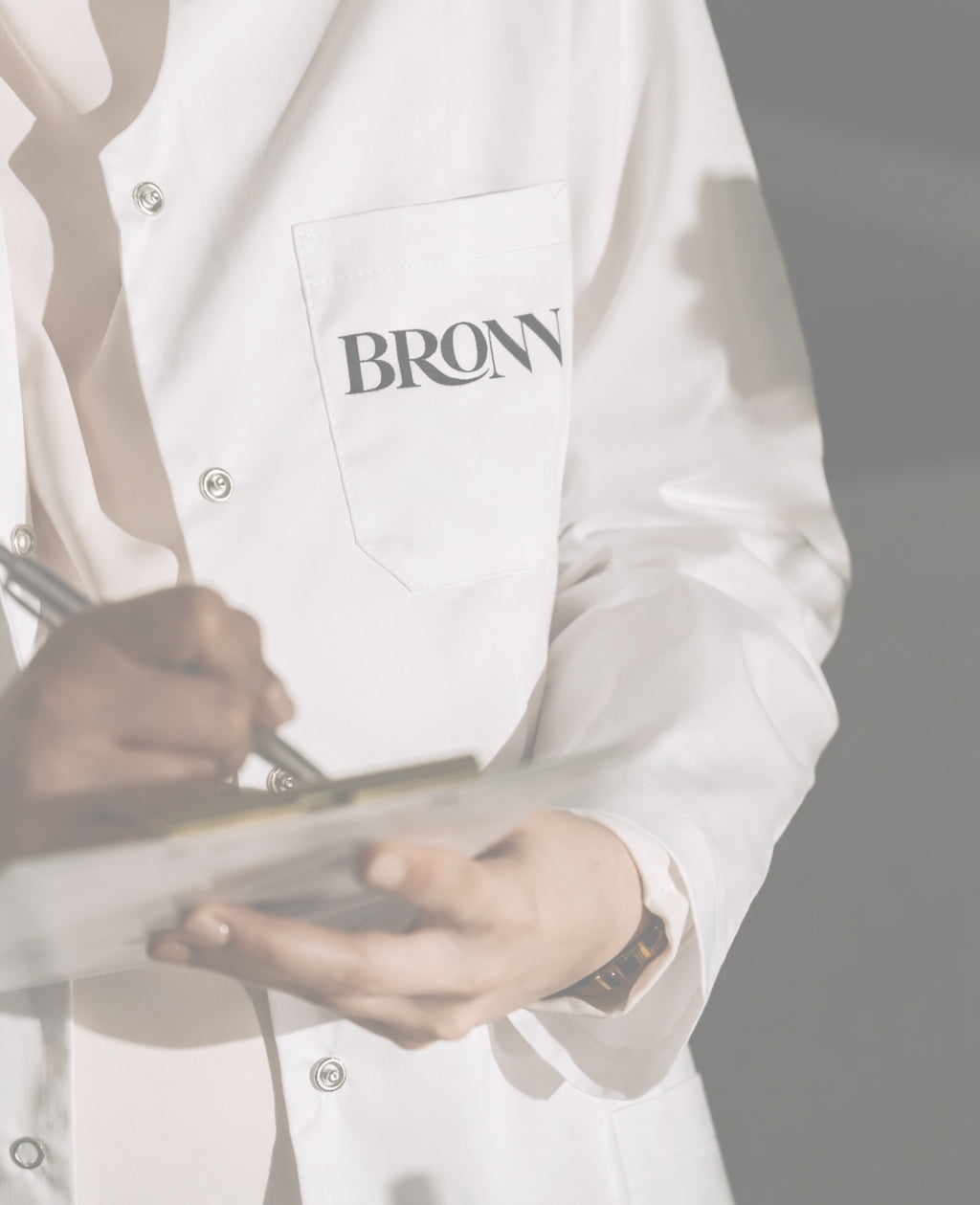 Person wearing a white coat with 'BRONN' printed on it, holding a tray.