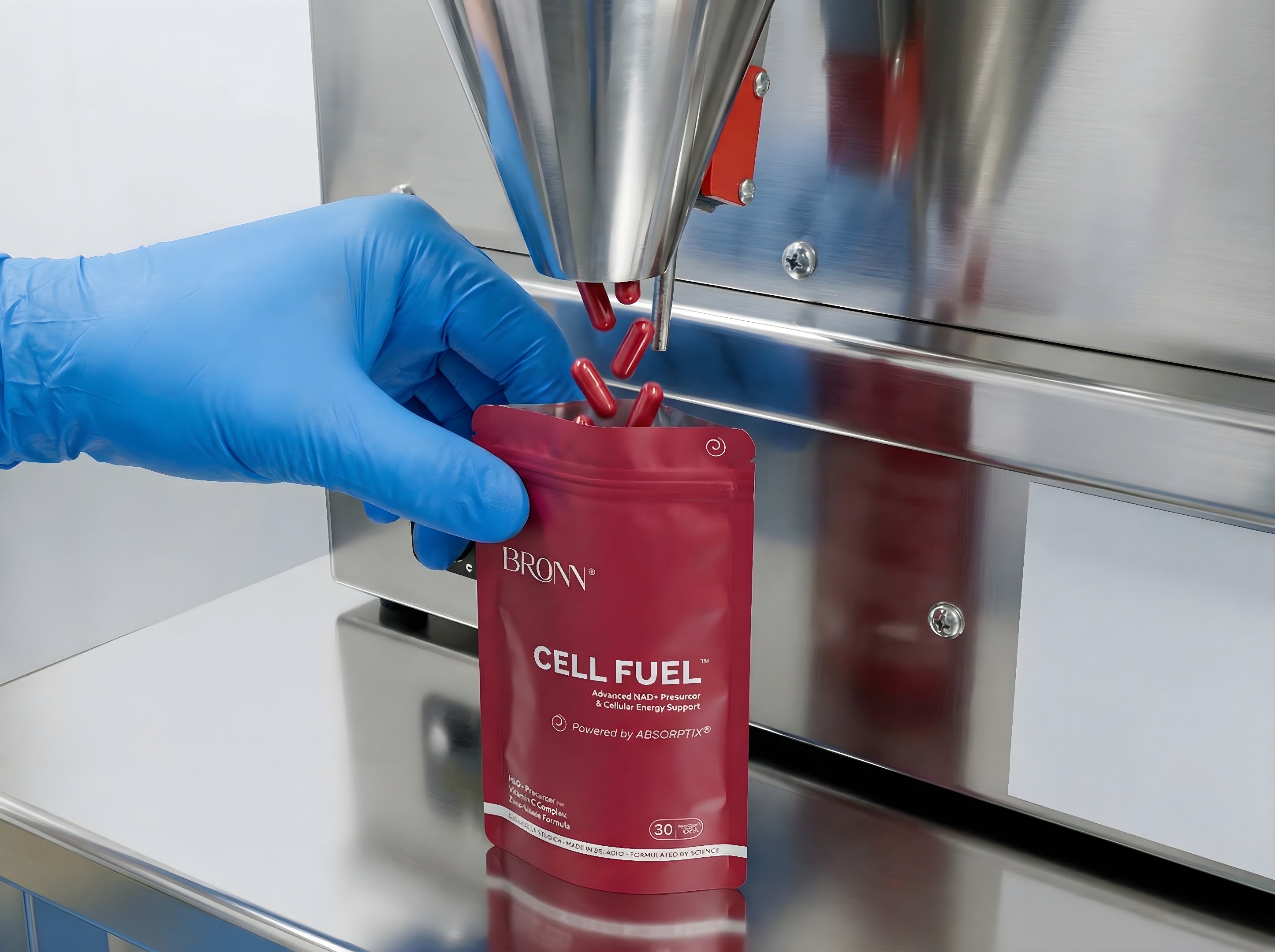 Red BRONN CELL FUEL package being filled with a tool, against a metallic background.